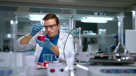 Chemist-studying-liquid-in-glass-flask-at-modern-lab.-Laboratory-worker
